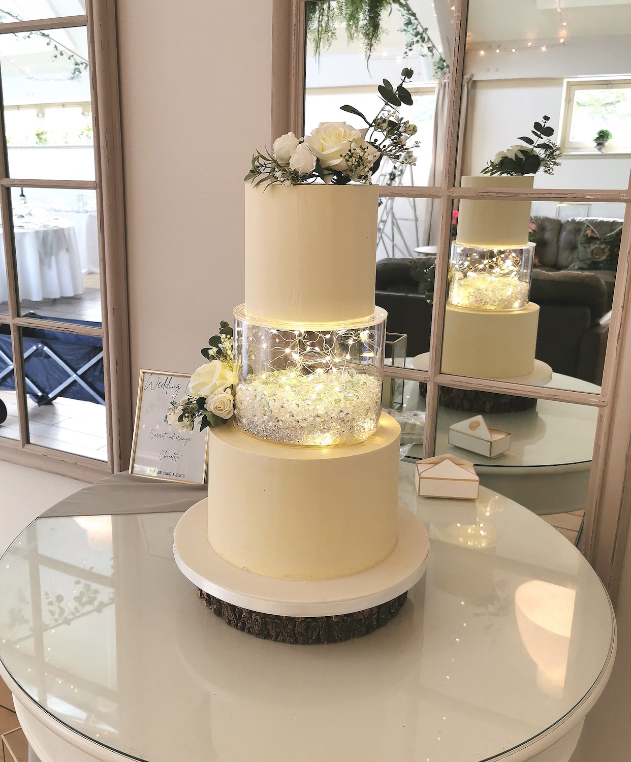 elegant simple white wedding cake with white flowers and see through layer with lights